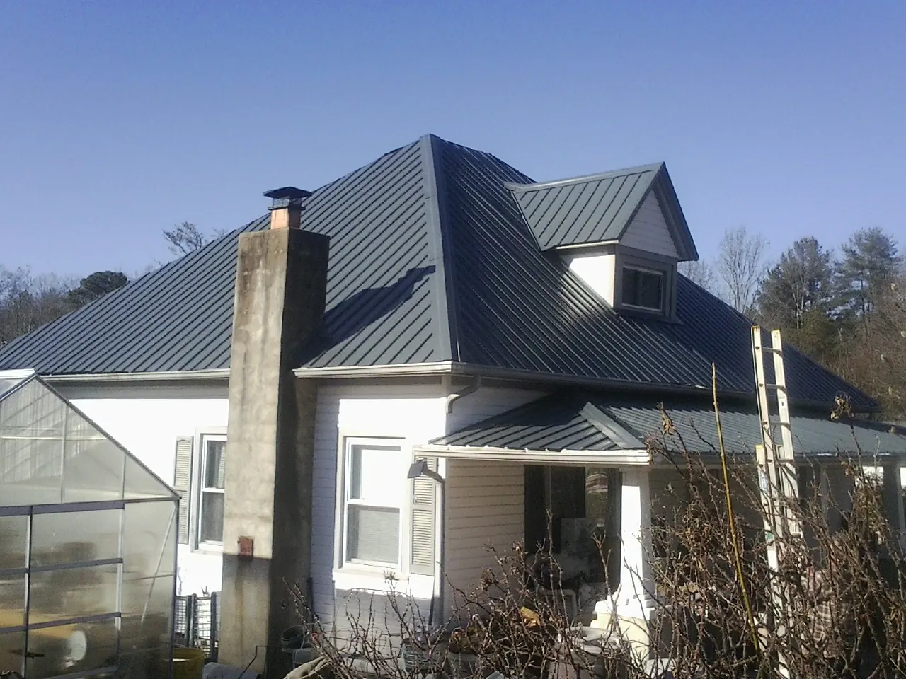 Dark blue standing seam metal roof on a white farmhouse with dormer — Slate & Tile Roof Repair by Roofing Brothers in Treynor