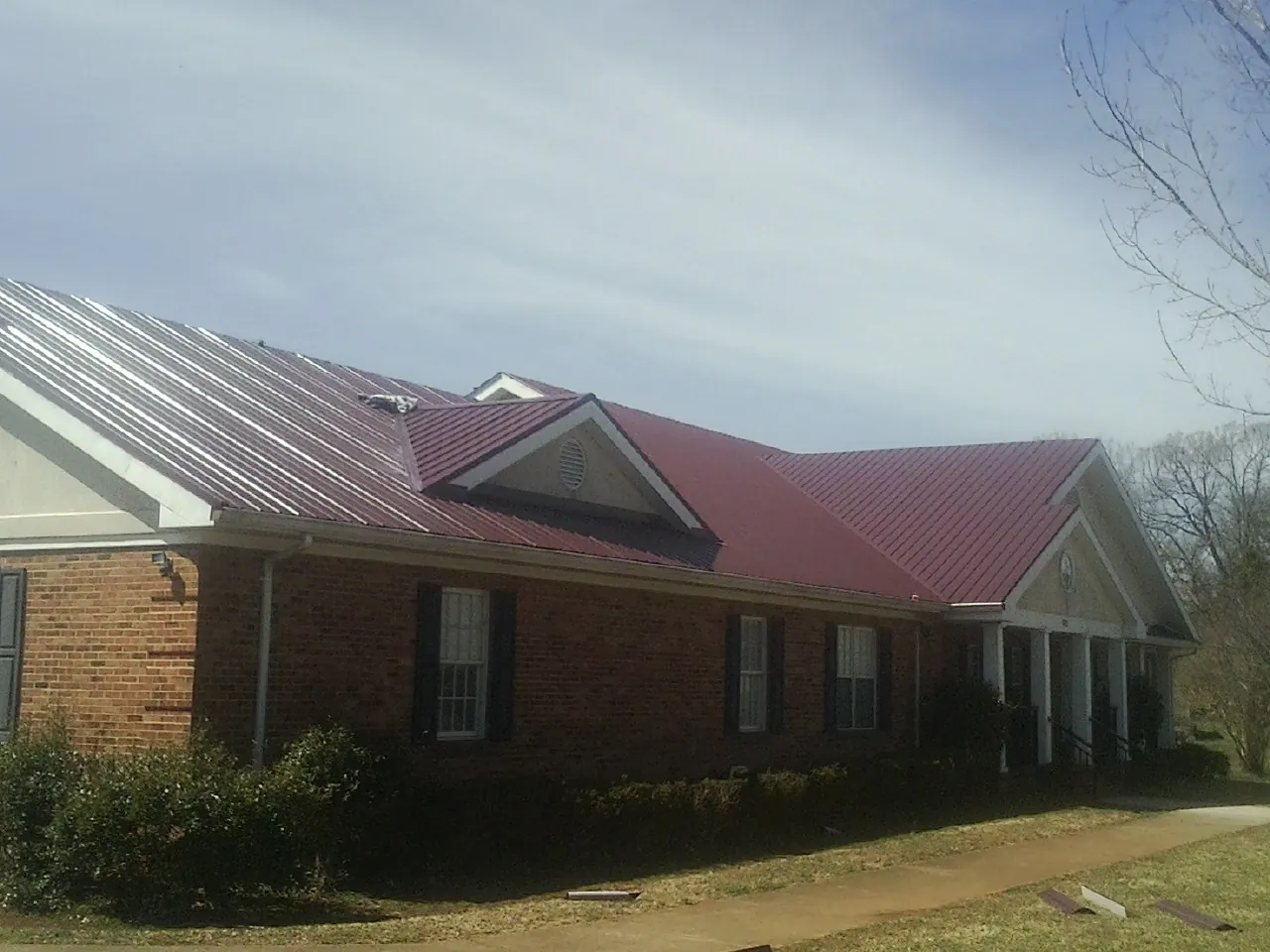 Red metal roof with gabled entries on a long brick building, from a Hail Damage Roof Repair job in Treynor