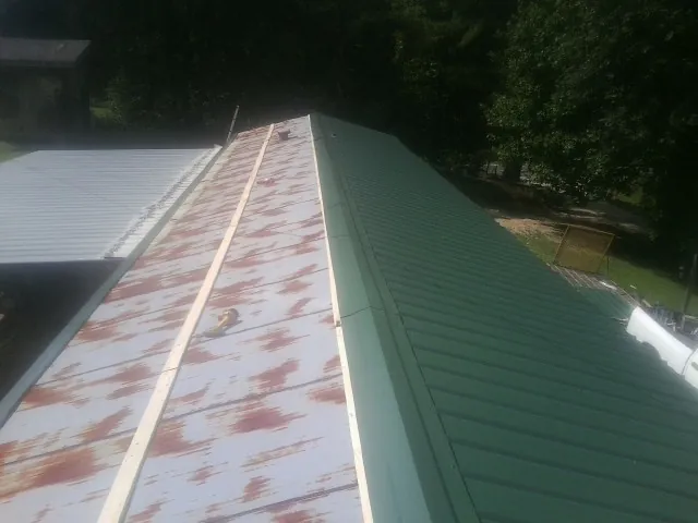 Old rusted panels beside newly installed green metal roofing — Wind Damage Roof Repair by Roofing Brothers in Treynor