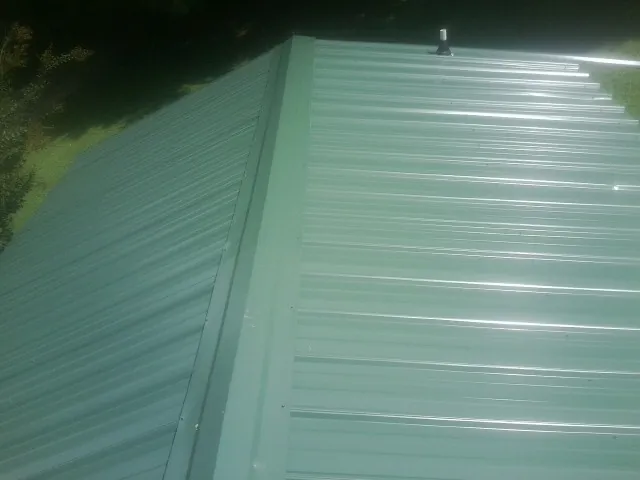 New green metal panels meeting at the ridge of a roof — Flat Roof Repair work by our crew in Treynor