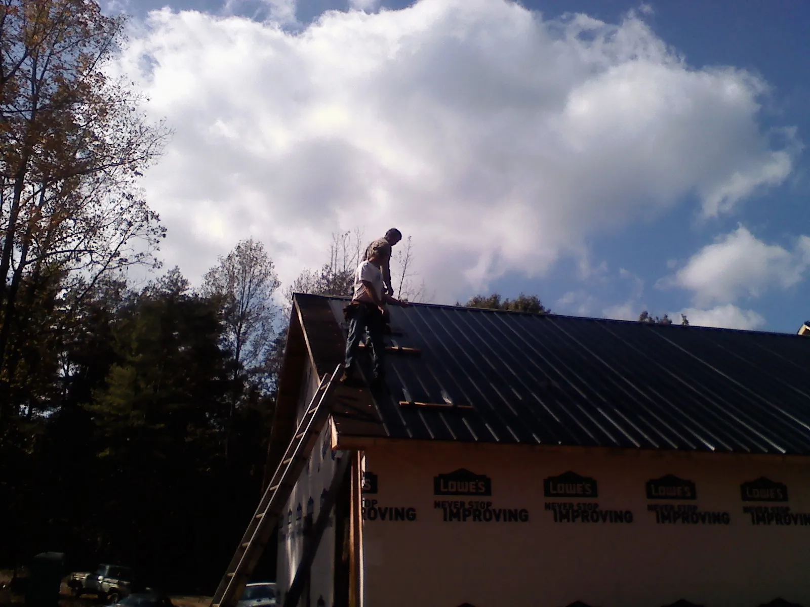 Roofer fastening dark metal panels high against a cloudy sky, from a Roof Inspection job in Treynor