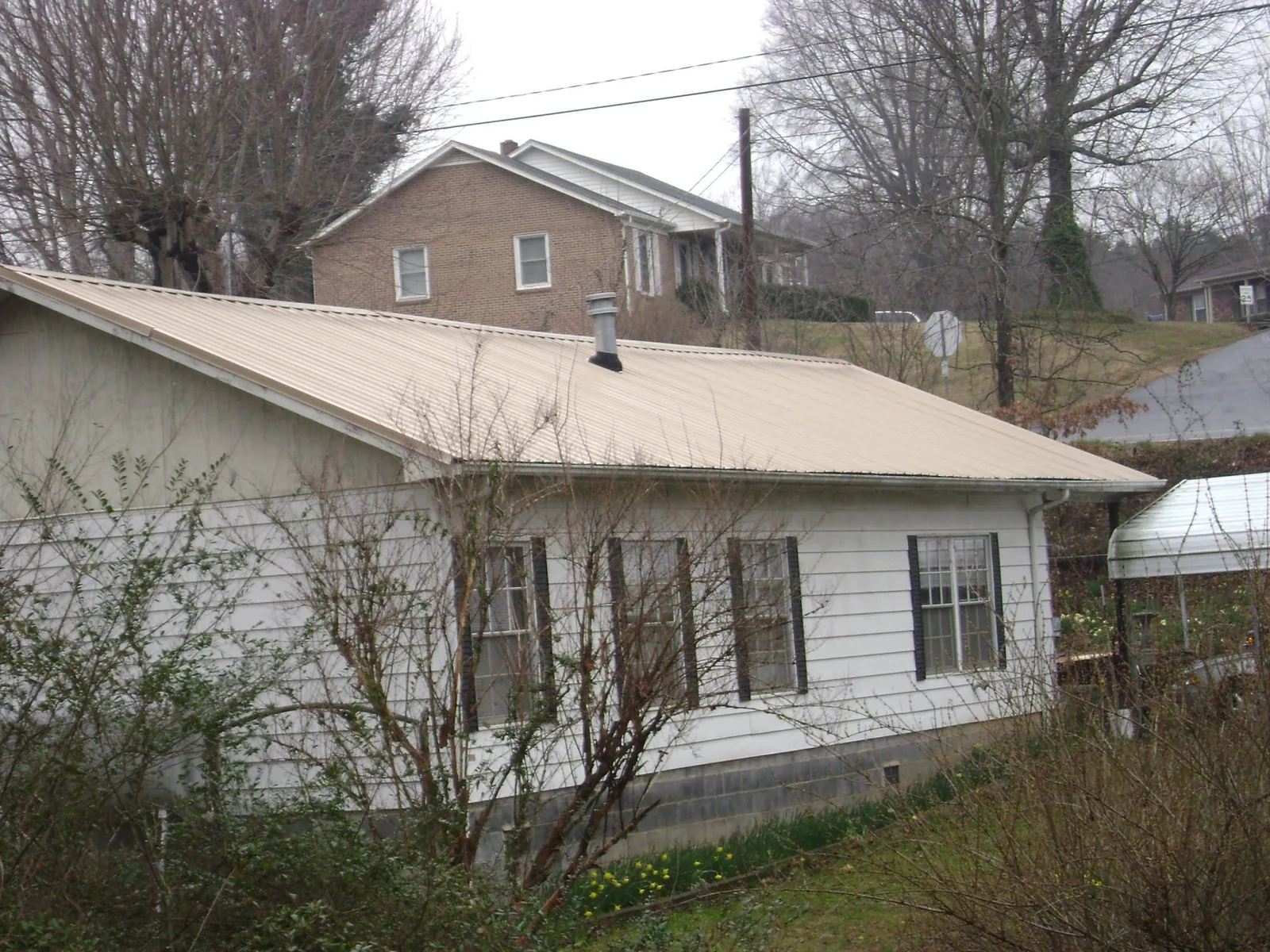Tan metal roof on a white sided house set into a hillside — Commercial Roofing by Roofing Brothers in Treynor